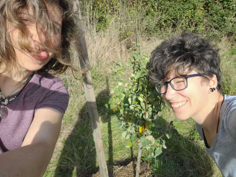 Vanessa et Mathilde souriantes devant leur poirier 'Conférence' nouvellement planté, le premier arbre de leur projet de jardin forêt, automne 2022.